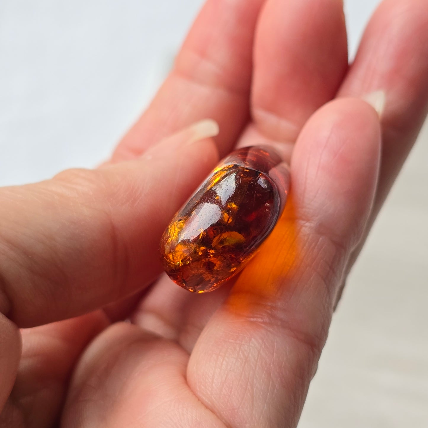 Hand holding a transparent amber stone against a neutral background