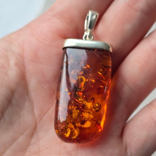 Amber pendant with silver setting held in a hand against a neutral background