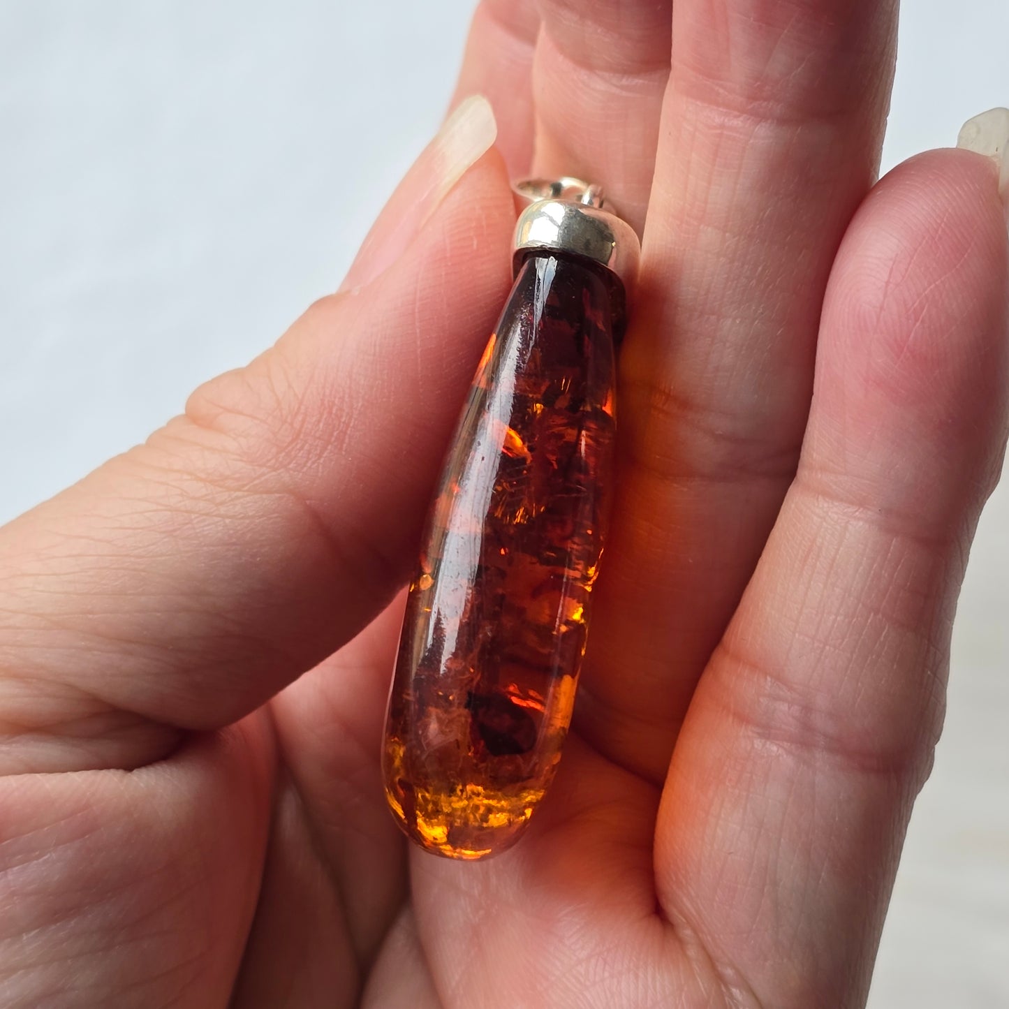 Amber-colored pendant held in a hand against a neutral background