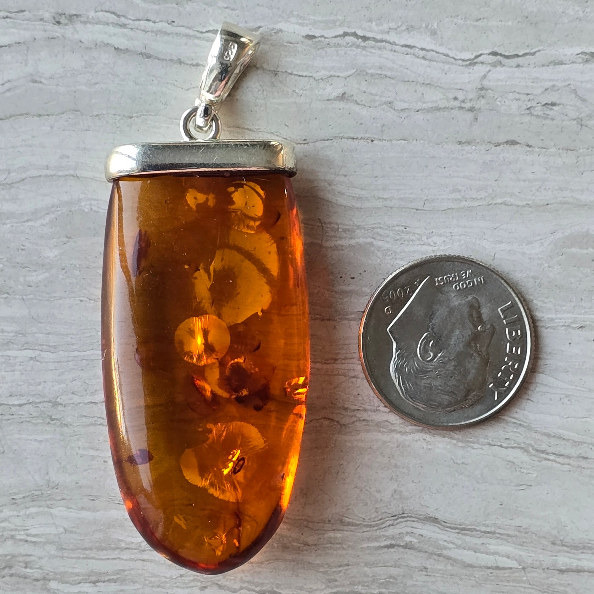 Amber pendant with silver setting next to a U.S. dime