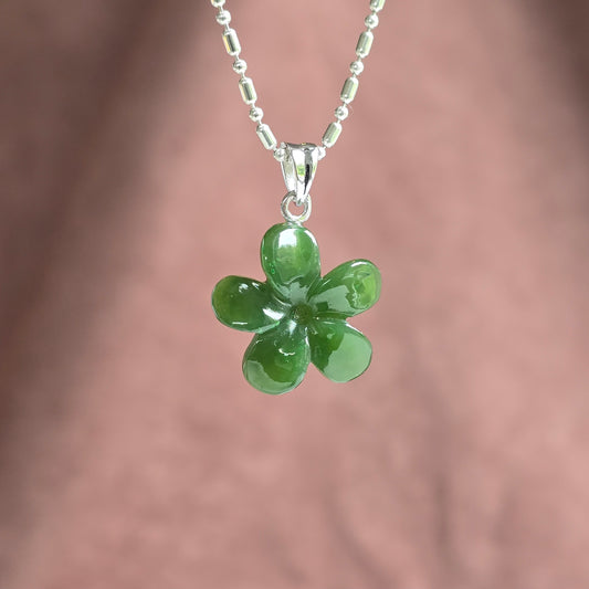 A silver beaded chain necklace with a glossy green five-petal flower pendant, shown against a soft, blurred pinkish-brown background.
